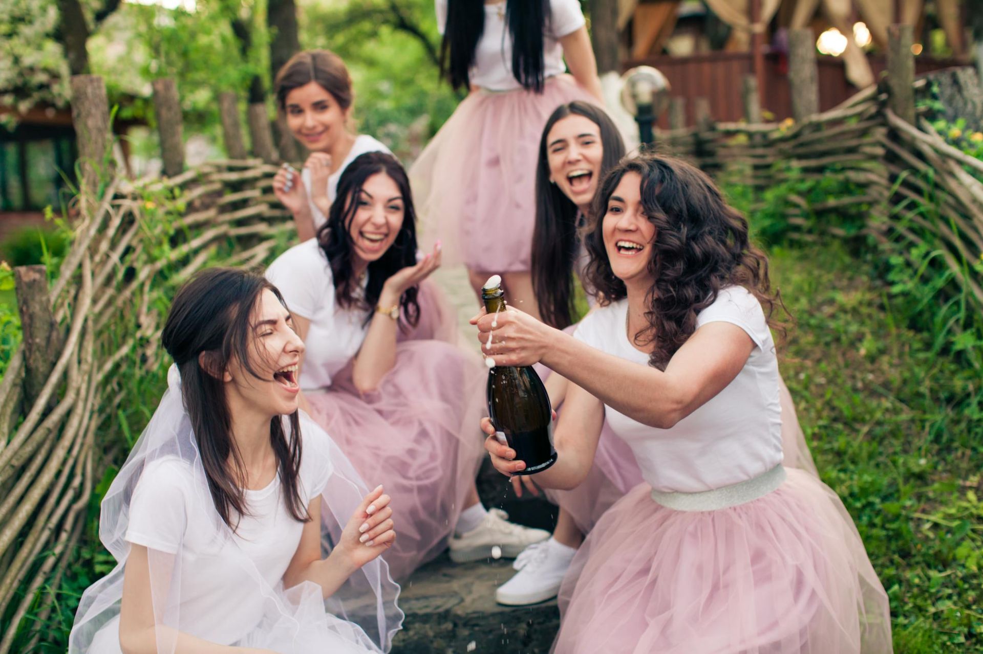 Dziewczyny na wieczorze panieńskim otwierają szampana w&nbsp;ogrodzie